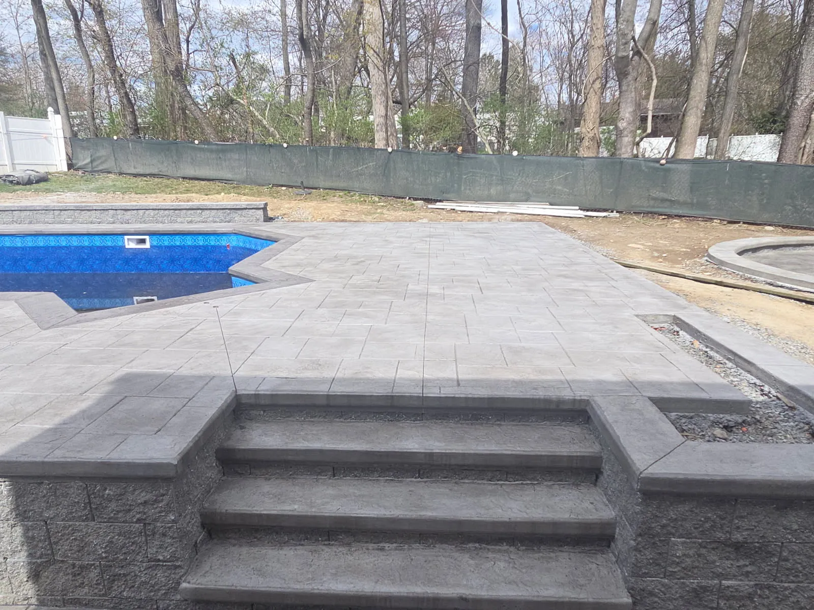 Stamped concrete pool deck with a raised block wall and steps under construction